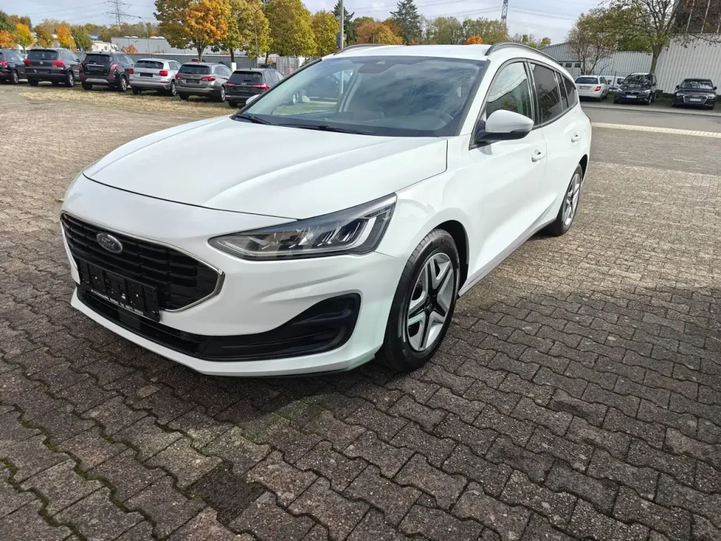 Weißer Ford Focus Cool Klima LED Shz PDC Airplay Winterpaket Kombi von vorne rechts, mit LED-Scheinwerfern und schwarzen Akzenten am Stoßfänger.