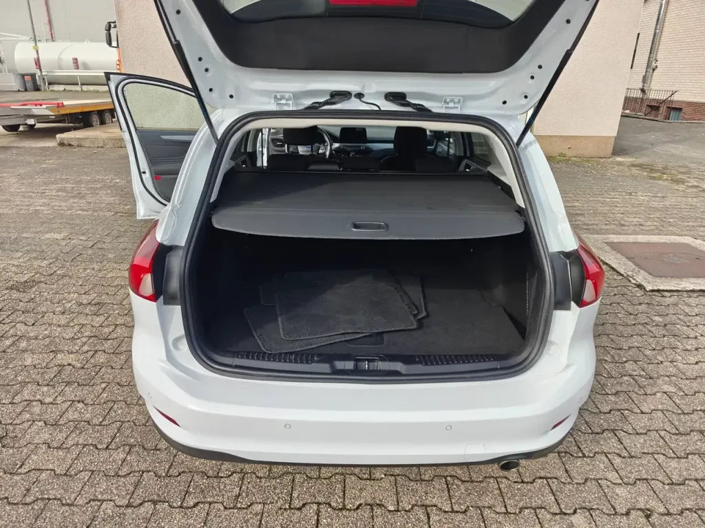 Kofferraum mit Ladeabdeckung und Fußmatten, geöffnete Heckklappe, weißer Ford Focus Cool Klima LED Shz PDC Airplay Winterpaket.