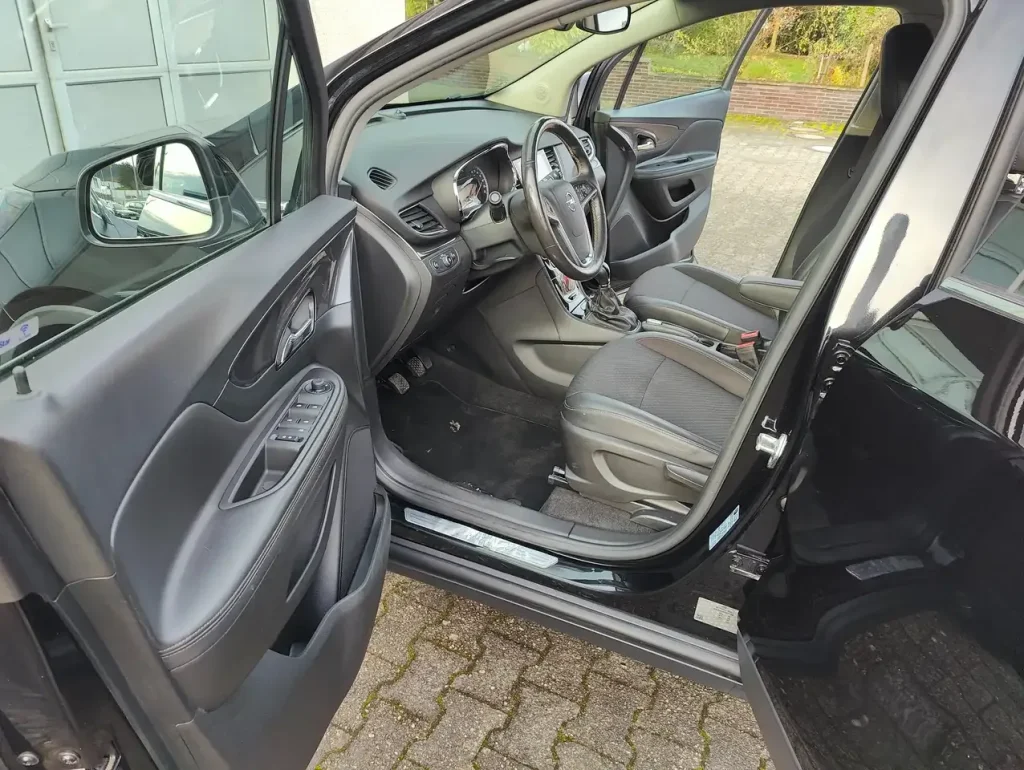 Opel Mokka X Innovation Start/Stop Fahrerseite mit offenem Tür, Lenkrad, Armaturenbrett und Vordersitzen in Schwarz.