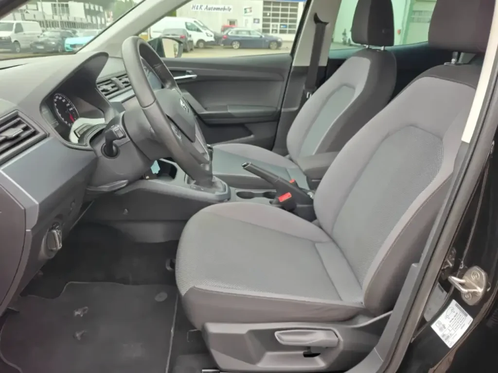 Innenraum mit Fahrer- und Beifahrersitz des Fahrzeugs SEAT Arona Style, graue Stoffpolsterung, Lenkrad und Mittelkonsole sichtbar