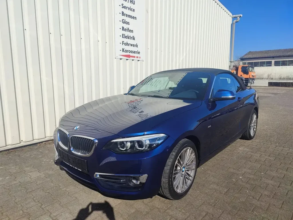 BMW 218 218 i Luxury Line LED Leder Alu Shz PDC, dunkelblauer Cabrio mit geschlossenem Verdeck, Front- und Seitenansicht.