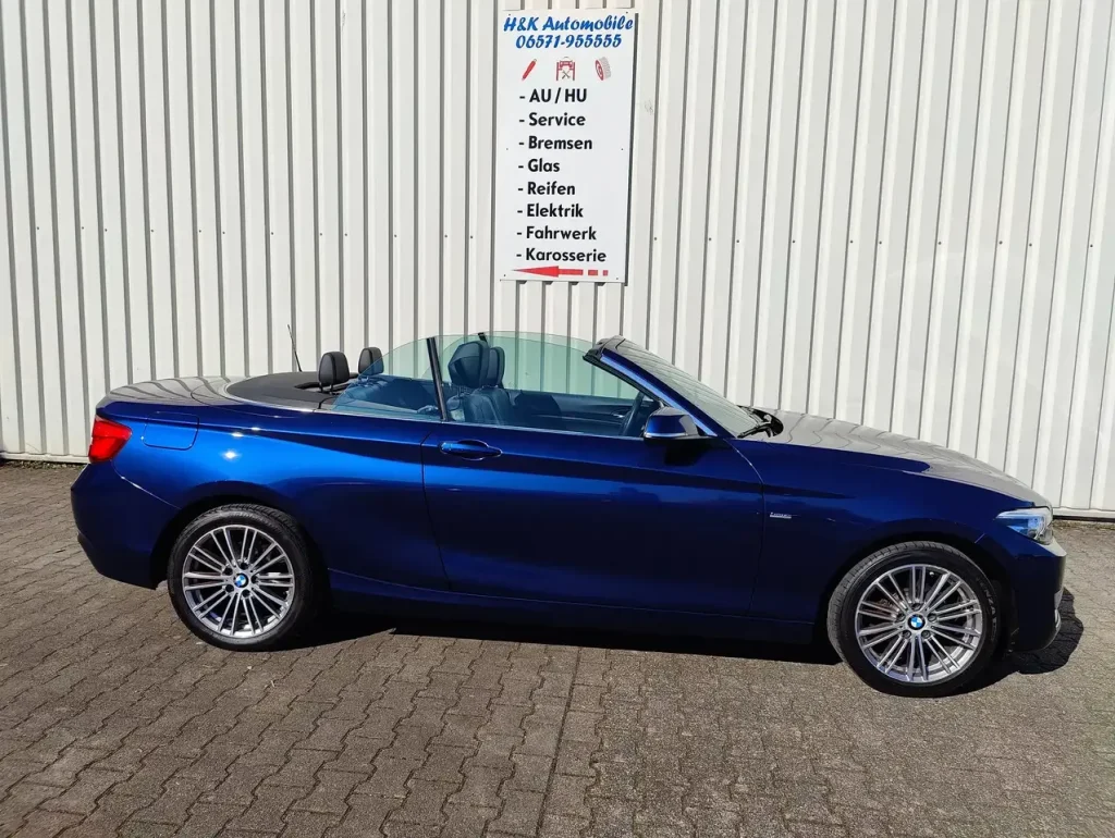 BMW 218 218 i Luxury Line LED Leder Alu Shz PDC Cabrio in Blau, Seitenansicht mit geöffnetem Verdeck und sichtbaren Leichtmetallrädern.