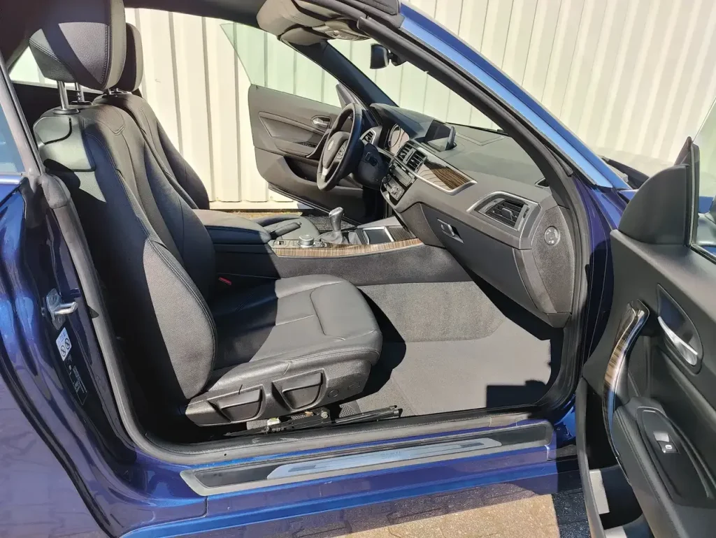 Innenraum mit offenem Fahrertür, schwarzem Ledersitz und Armaturenbrett des BMW 218 218 i Luxury Line LED Leder Alu Shz PDC.