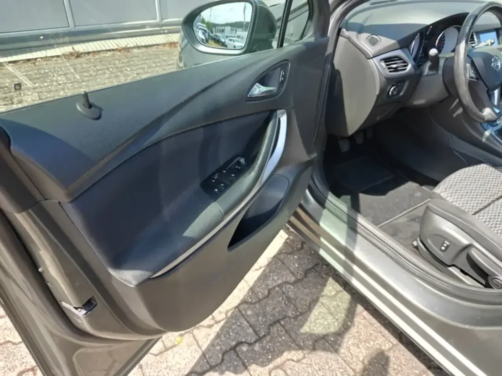 Opel Astra Edition Start/Stop Winterpaket 1.Hd Navi Fahrertür mit Türverkleidung, Fensterheberschaltern und Teilansicht des Innenraums mit Sitz und Lenkrad.